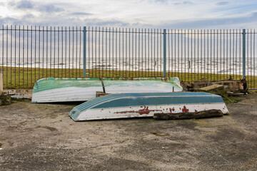 Old Derelict White and Green Painted Wooden Rowing Boats Upside Down on Concrete Dock In Front of...