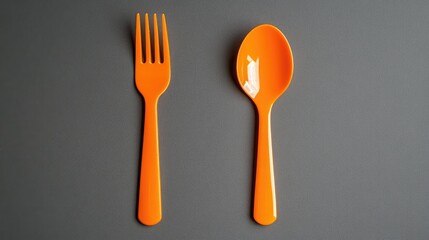 Orange plastic fork and spoon on dark gray background with Copy Space for text placement