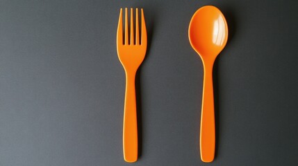 Pair of orange plastic fork and spoon on a dark surface with copy space for text or branding