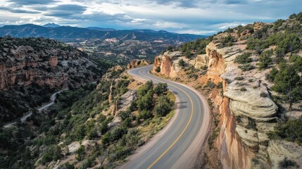 Winding mountain road through rocky terrain with lush greenery and distant hills under a cloudy sky Copy Space