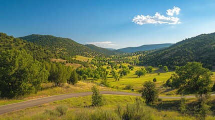 Naklejka premium Scenic landscape view of rolling green hills and winding road under clear blue sky with fluffy clouds and ample copy space.