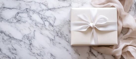 Gift box with white ribbon on marble surface with fabric Copy Space