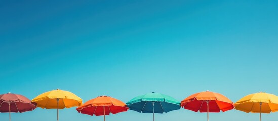 Colorful beach umbrellas swaying in the wind under a clear blue sky with ample empty space for text or promotional content.