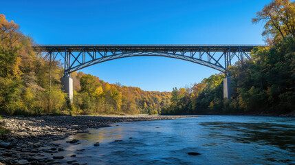 Fototapeta premium Low-Angle Shot of a Modern Steel Bridge Spanning Over a River Beneath a Clear Blue Sky, Symbolizing the Achievement of Civil Engineering Design and Innovation