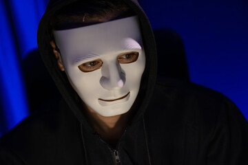 White criminal anonymous mask installing coding password encryption by programming hack, trying to make insecure thorough privacy taking massive database on computer for ransom to company. Pecuniary.