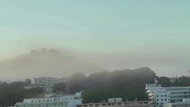 Fog at dawn spreads across a hill and houses. Tenfold acceleration. Majorca Island. Spain.
