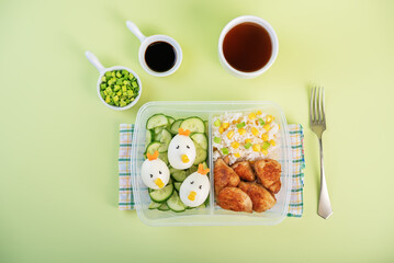Bento box with rice, fried meat slices, cucumber and eggs in the form of funny chickens