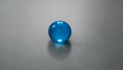 무채색의 회색 배경 위에 하나의 푸른 구슬이 반짝이며 중앙에 놓여 있다. 구슬은 투명한 빛을 반사해 강조된다