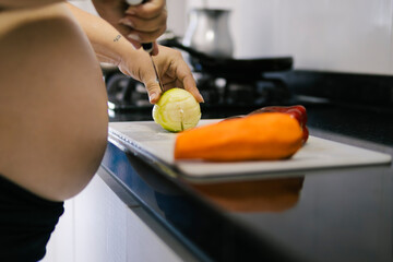 Pregnant colombian woman cutting lemon in kitchen with vegetables