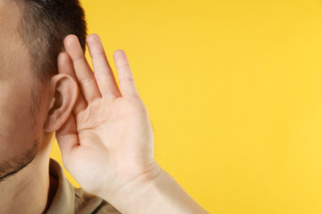 Man showing hand to ear gesture on orange background, closeup. Space for text