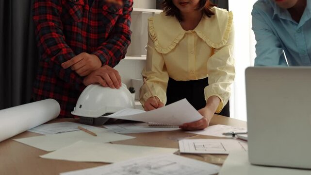 Architect and safety engineer discussion about building blueprint displaying on laptop on table with architectural document and wooden block scatter around at modern office. Closeup. Delineation.