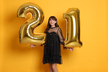 Coming of age party - 21st birthday. Young woman holding number shaped balloons on yellow background