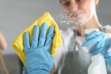 Woman using cleaning product while wiping mirror with rag indoors, closeup