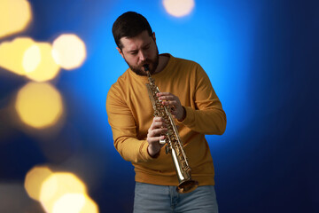 Naklejka premium Professional musician playing soprano saxophone on blue background with blurred lights. Bokeh effect