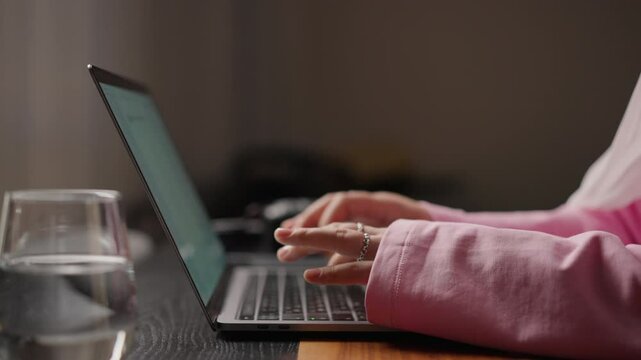Close-up of Muslim woman in pink sleeves typing steadily on laptop. Setup emphasizes focus and simplicity in a modern home workspace. Concept of multitasking and remote work at home