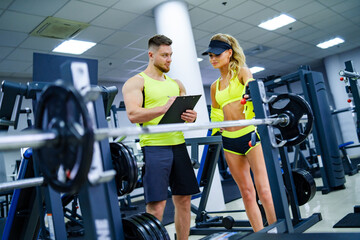 Fitness coaching session at the gym. A fitness coach guides a female client in workout techniques inside a gym. They discuss training routines and goals.