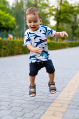 Fototapeta premium Young child joyfully jumping in park. A young boy plays in a park, joyfully jumping along a path surrounded by greenery on a sunny day.