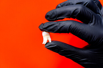 Tooth extraction at the dentist. A gloved hand holds an extracted tooth against a vivid orange...