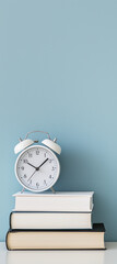 alarm clock sits atop three books, with a pastel blue wall in the background.
