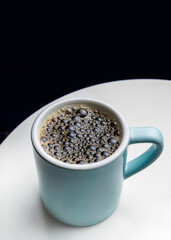 Blue mug with filtered coffee. The surface of the coffee is covered with bubbles, indicating a freshly brewed drink. Menu for a cafe, restaurant. Small business. Black background, space for text