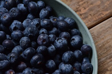 A full bowl of bilberries fragment on a wooden table top view close up macro.