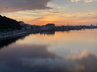 Urban waterfront sunset scene with church, reflections on calm water, and a prominent building...