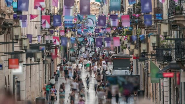 Tourists and locals walking and shopping in Rue Sainte-Catherine timelapse, Bordeaux, France. The longest pedestrian street in the country. Atmosphere of urban life. Colorful flags decorate the street