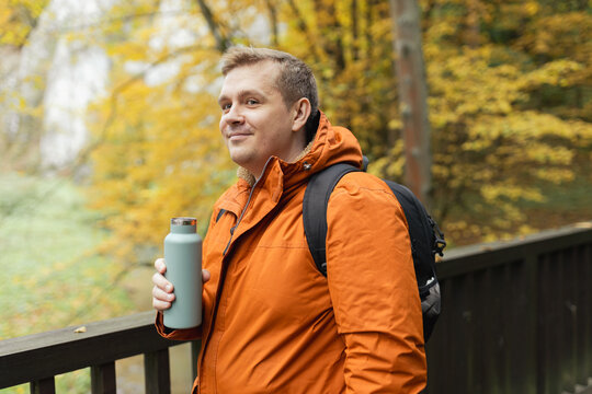 30s Plus size male with backpack smiling outside on an adventure. Hiking, lifestyle, adventure and tourism concept. Young man standing on the bridge in woodland, autumn time.