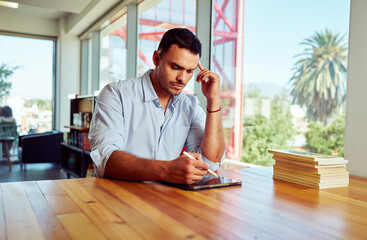 Young businessman using stylus pen on digital tablet, concentrating on his work in a bright, modern...