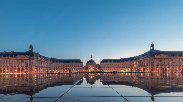 Place de la Bourse and Miroir d'eau day to night transition panoramic timelapse in Bordeaux, France, reflecting illuminated architecture. Landmark and the fountain with traffic and tram passing by