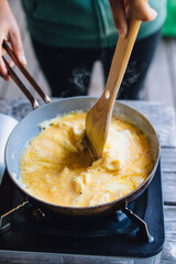 woman making scrambled eggs in frying pan on outdoor burner while camping