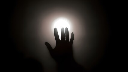 A man's hand reaches out to the light in the darkness, his silhouette clearly outlined against a distant beam of warm light. The scene captures a moment of hope and aspiration.