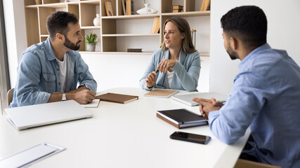 Group of diverse business partners negotiate in boardroom, listen speech of middle-aged female boss talking about strategy, discuss partnership, upcoming projects details or corporate goals. Briefing
