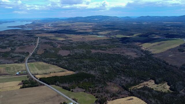 High‑altitude drone view of the Matapedia Valley showing autumn fields, a winding rural road, Lake Matapedia, and distant Appalachian Mountains in Quebec, Canada