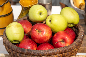 Green and red apples in a rustic wicker basket on a laid table
