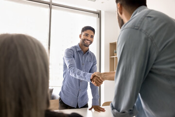 Young businessman greeting new team member, client, or partner, shake hands gathered in boardroom, showing acknowledgment and respect, confirming commercial deal, partnership, or mutual understanding