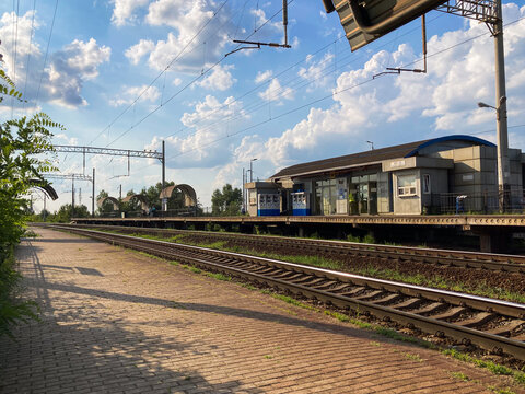 Image of a railway station with multiple tracks, partially hidden train, small blue-white building, partly cloudy sky, ruralsemi-rural setting, brick platform, lamppost, - Kyiv, Ukraine 06-02-2024