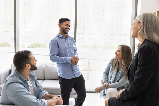 Group of laughing diverse company employees talking during break, listening funny jokes or anecdote of young cheerful Arabian male colleague, looking carefree, and untroubled during pause at workplace