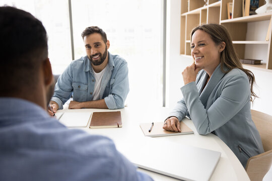 Teammates sit at conference table take part in collaborative or brainstorming session in office, smile, enjoy talk, share creative ideas, participate in briefing event, discuss recent project details