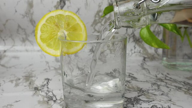 Closeup of tap water poured into glass lemon slice on marble clean white background. Purity, nature, health, diet, detox