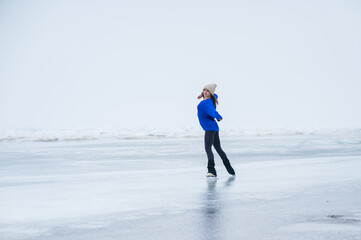 Caucasian woman in a blue sweater is skating on a frozen lake. The figure skater performs the program.