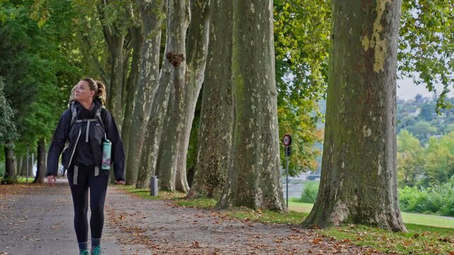 Backpacking woman walking on a tree lined park path in slow motion, Koblenz, Germany