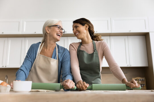 Cooking with mom. Two happy diverse age women older adult mother young grown up daughter laugh having fun roll dough cook pizza at home kitchen together talk spend time baking cookies by family recipe - Powered by Adobe