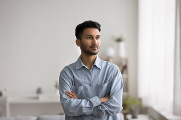 Everything start from idea. Confident thoughtful young man small business owner stand indoors with arms crossed look away on distance create work plans ponder on startup visualize way to achieve goal