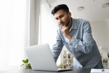 Pensive serious millennial male freelance worker entrepreneur working from home office stand by...