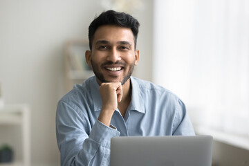 Success in profession. Portrait happy smiling young man office worker freelancer sit at workplace by notebook. Friendly male consultant advisor insurer look at camera feel satisfied glad enjoy his job