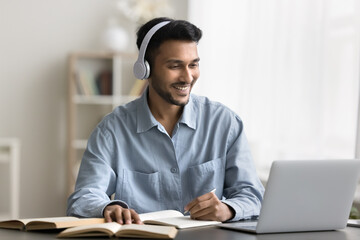 Getting knowledge online. Cheerful smiling young male student wear digital earphones watch video...