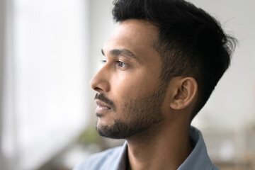 Obraz premium Business vision. Closeup shot face in profile serious pensive young adult man standing close to window looking away think of office career new job opportunities professional growth project development