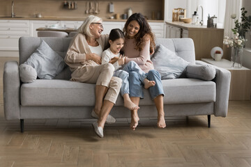 Carefree weekend. Laughing 3 generation family tickle on couch joyful elderly mum grandma playing...