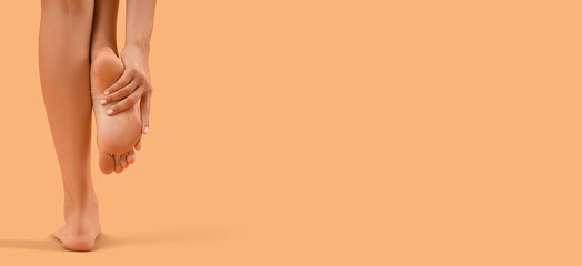 Young woman massaging foot on light background with space for text